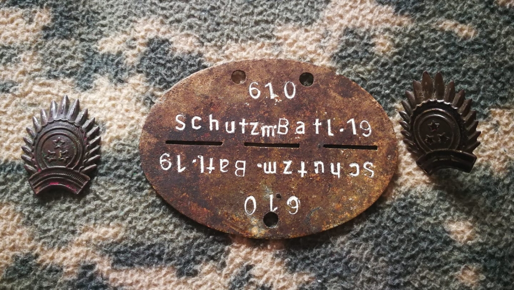 Identifikācijas žetons 
“19. Latgales policijas bataljons”. Tam blakus - pirmās Latvijas Republikas armijas kokardes saulītes - 30.gadi. “Tādas, tāpat kā tālaika pulka zīmes, nēsāja gan policijas bataljona vīri, gan leģionāri,” stāsta Māris Jurciņš.                    
Autors: no personiskā arhīva