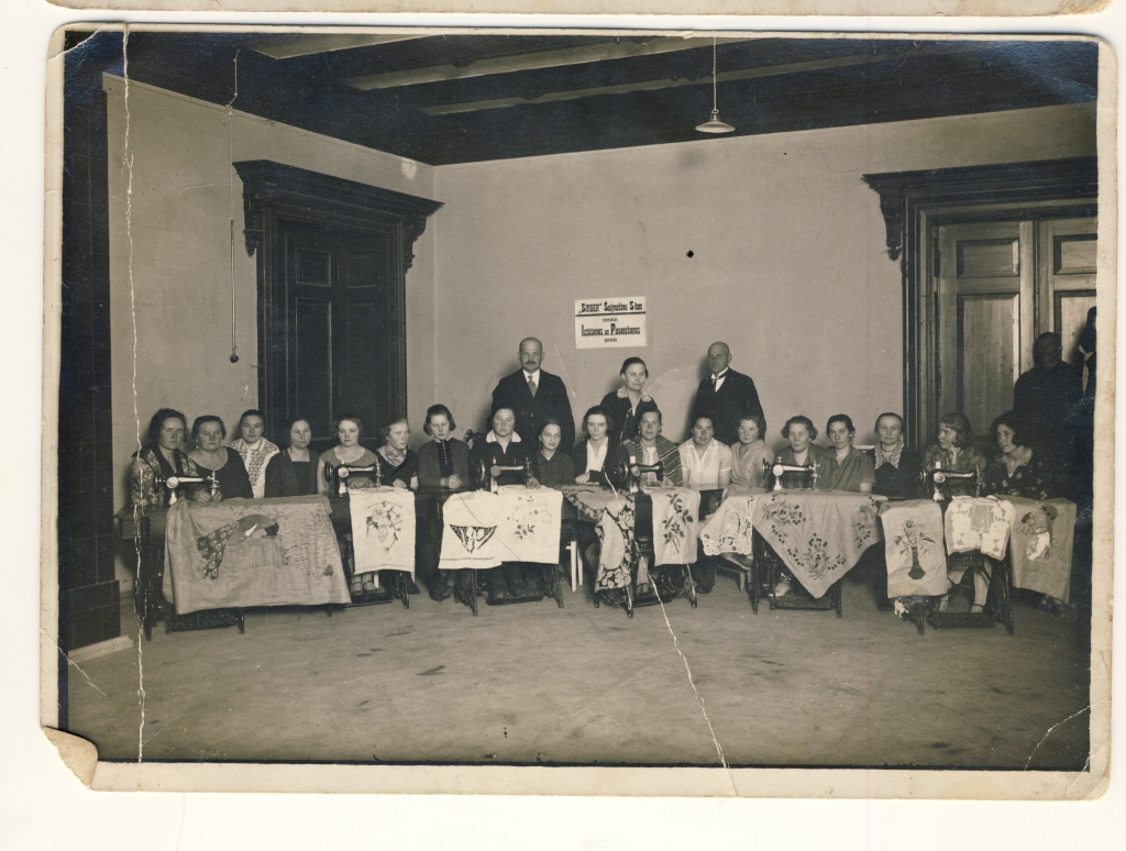 Jaungulbenes pilī rokdarbnieces rāda, ko spēj izšūt ar “Singer” šujmašīnu. Starp izstādes dalībniecēm arī Milda Cinkuse. Apmēram 1928.gads. 
Autors: no Antras Bušujevas arhīva