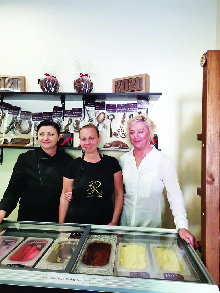 Trikātas šokolādes meitenes. Aiz viņām redzami šokolādes darbarīki, priekšā – gardais saldējums, ko arī ražo uz vietas. Vēl veikaliņā var nopirkt šokolādes trifeles, medaljonus, kraukšķus, augļus šokolādē un citus gardus našķus.  
Autors: Pārsla Konrāde