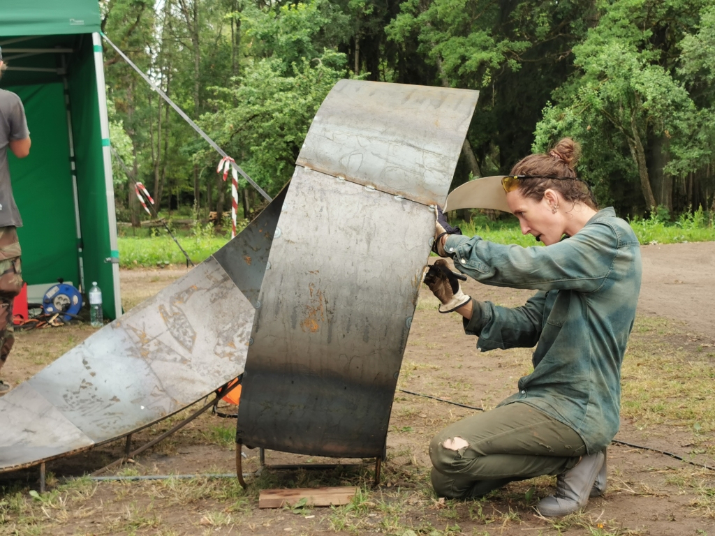 Blakus Stāķu parkam šīs nedēļas laikā, spītējot karstajai saulei, seši Latvijas Mākslas akadēmijas (LMA) topošie un esošie mākslinieki savieno, metina, griež un fleksē metāla konstrukciju, kam “Dzirksteles” ierašanās brīdī jau bija pamanāmas iecerētās aprises. LMA Metāla dizaina katedras pasniedzējs Arvīds Endziņš puspajokam saka – “cīņa lielāka mums ar sauli, nekā pašu tēraudu.” 3.kursa studente Anastasija Bikova (attēlā) gan izveidoja skici, kas uz “sirdi” liek paskatīties no dažādiem rakursiem, ļauj tajā pabūt un pieskarties, gan piedalās vides objekta izgatavošanā uz vietas.
Autors: Viktorija Slavinska-Kostigova