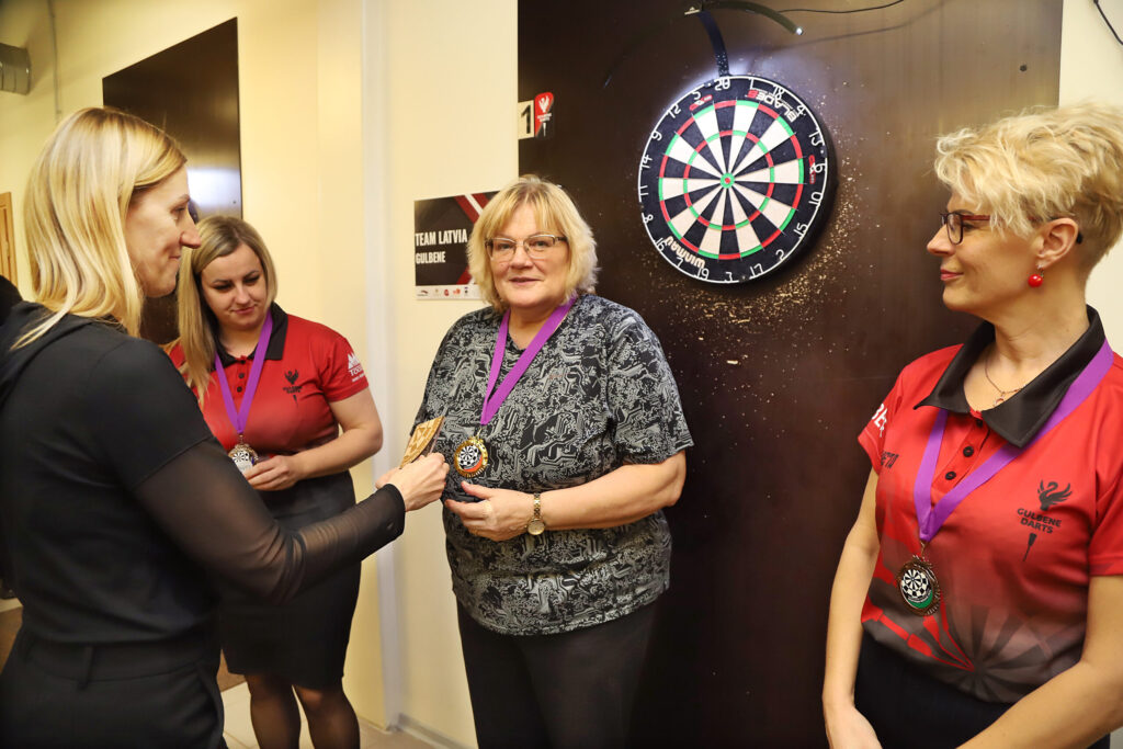 Sporta pārvaldes pārstāve Dace Anča (no kreisās) sveic šautriņu čempionāta uzvarētājas Līvu Kočāni, Maiju Ružāni un Inetu Ivašenko.
Autors: Foto: Gatis Bogdanovs